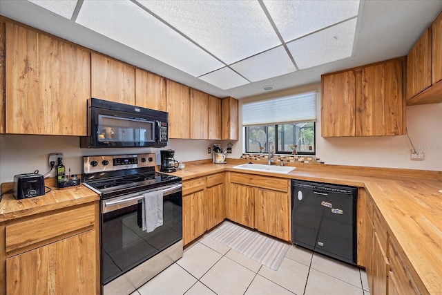 kitchen with black appliances, butcher block countertops, light tile patterned floors, and a sink