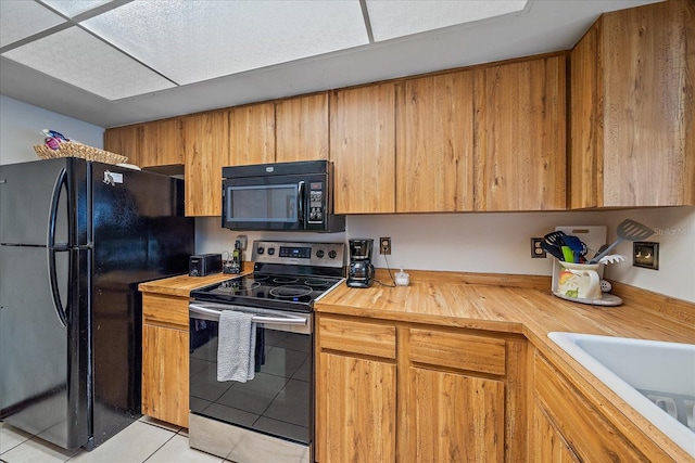 kitchen with a sink, wood counters, black appliances, and light tile patterned floors