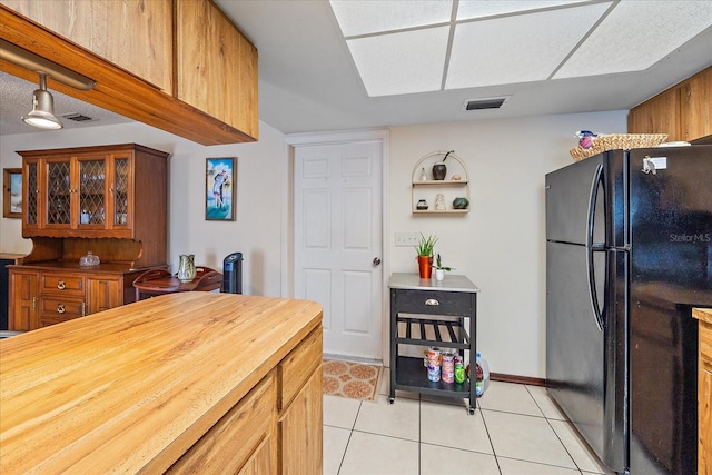 kitchen featuring light tile patterned floors, visible vents, wood counters, and freestanding refrigerator