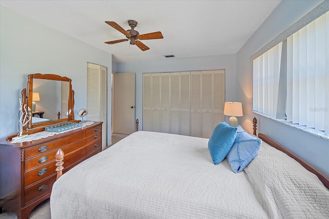 bedroom with a textured ceiling, ceiling fan, visible vents, and multiple closets