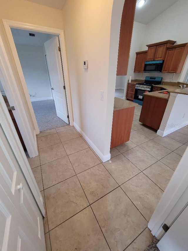 kitchen featuring brown cabinets, light countertops, light tile patterned flooring, black microwave, and stainless steel gas range oven