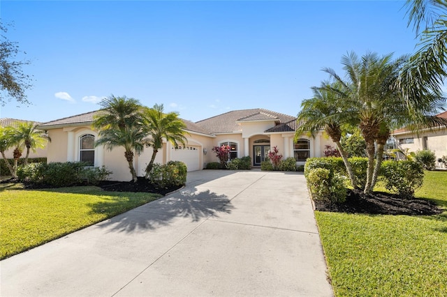 mediterranean / spanish house with an attached garage, a tile roof, driveway, stucco siding, and a front yard