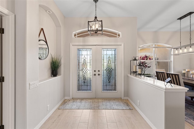 foyer entrance with a chandelier, french doors, wood finished floors, and baseboards