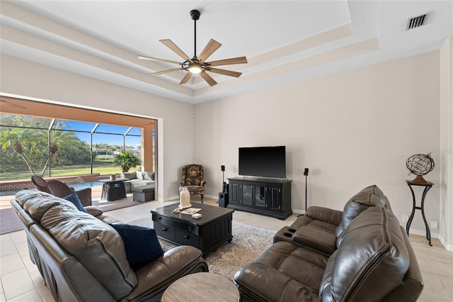 living area with a raised ceiling, visible vents, a sunroom, ceiling fan, and baseboards