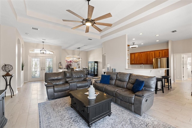 living room with arched walkways, light wood-style flooring, visible vents, french doors, and a raised ceiling