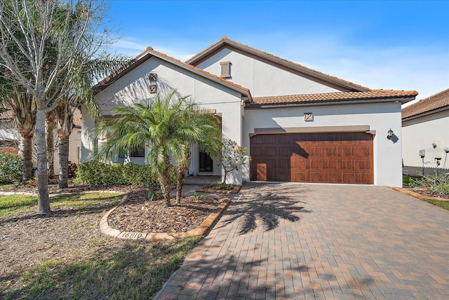 mediterranean / spanish-style house featuring a garage, a tiled roof, decorative driveway, and stucco siding