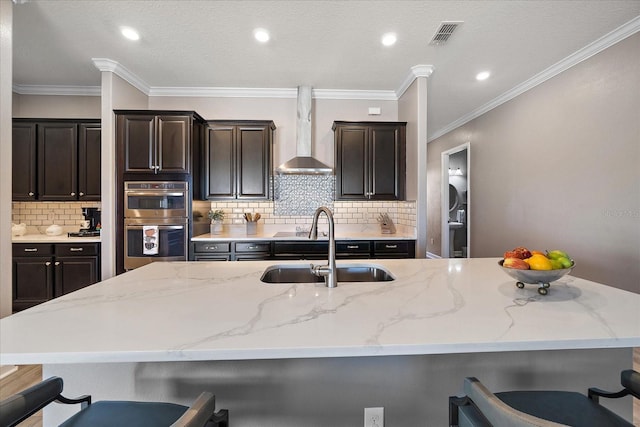 kitchen featuring double oven, wall chimney range hood, a kitchen bar, and a sink