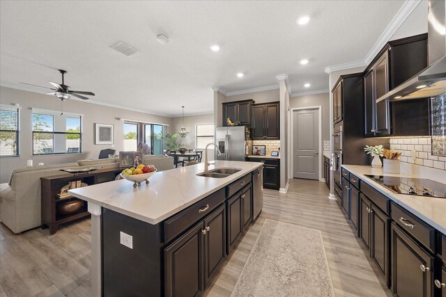 kitchen with a sink, open floor plan, light countertops, appliances with stainless steel finishes, and wall chimney exhaust hood