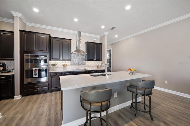 kitchen with a breakfast bar, visible vents, double oven, a sink, and wall chimney exhaust hood