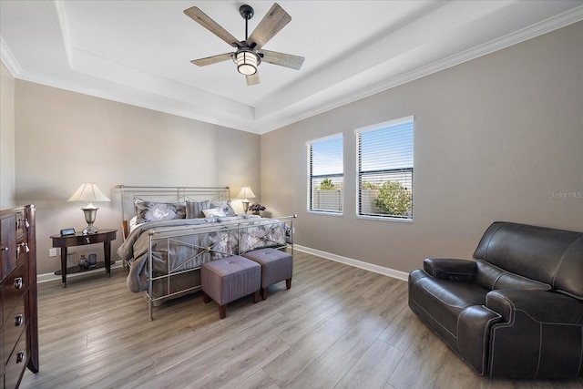 bedroom with light wood-style floors, a raised ceiling, and baseboards