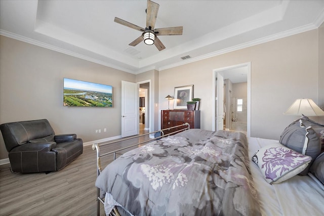 bedroom featuring a tray ceiling, visible vents, ensuite bathroom, light wood-style floors, and baseboards