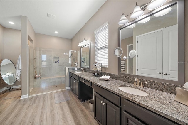 bathroom with double vanity, walk in shower, a sink, and wood finished floors