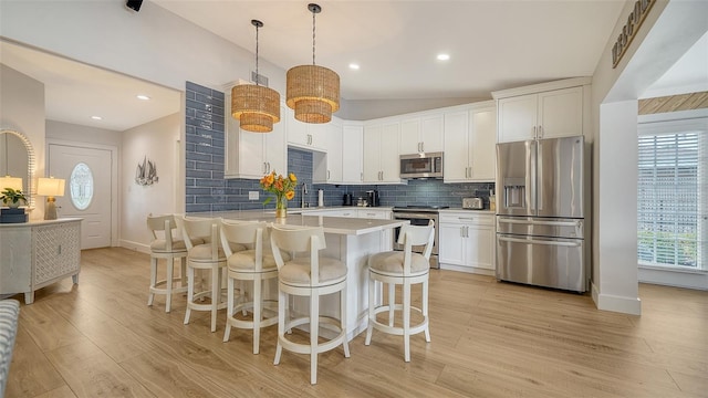 kitchen featuring decorative backsplash, white cabinets, stainless steel appliances, and a kitchen bar