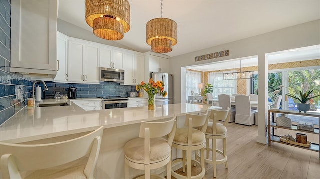 kitchen featuring a peninsula, stainless steel appliances, light countertops, pendant lighting, and tasteful backsplash