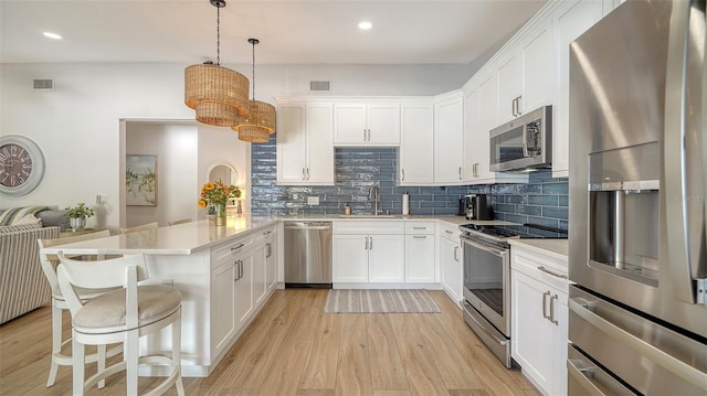 kitchen featuring a peninsula, light wood-style flooring, appliances with stainless steel finishes, white cabinetry, and tasteful backsplash