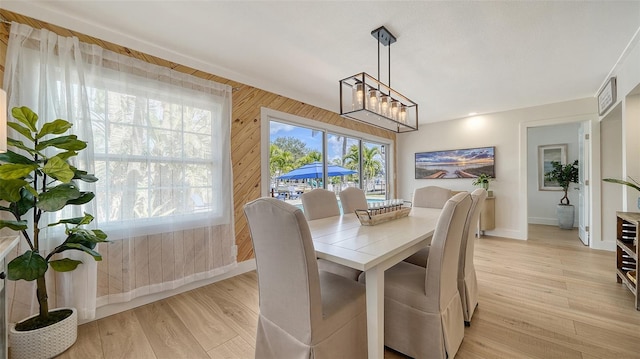 dining room featuring light wood finished floors, wooden walls, a chandelier, and baseboards