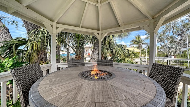 wooden deck with a gazebo, outdoor dining area, and a fire pit