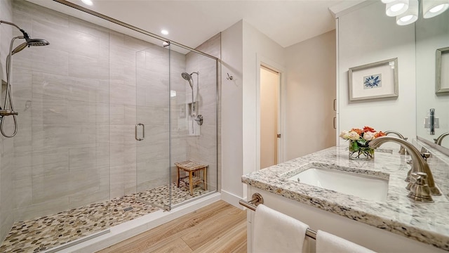 full bathroom featuring double vanity, a shower stall, wood finished floors, and a sink