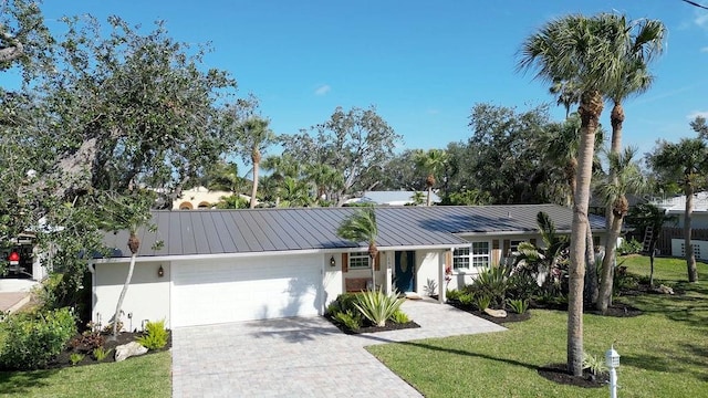 single story home with an attached garage, metal roof, a front lawn, and decorative driveway