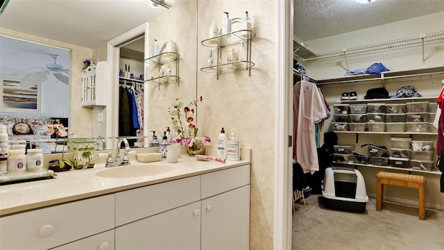 bathroom with a textured ceiling, a walk in closet, a ceiling fan, and vanity