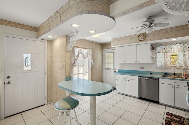 kitchen featuring light tile patterned flooring, white cabinetry, a sink, dishwasher, and wallpapered walls