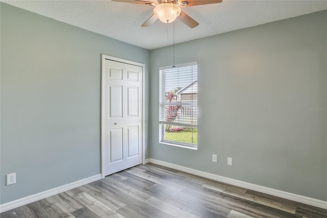 unfurnished room with a textured ceiling, ceiling fan, wood finished floors, and baseboards