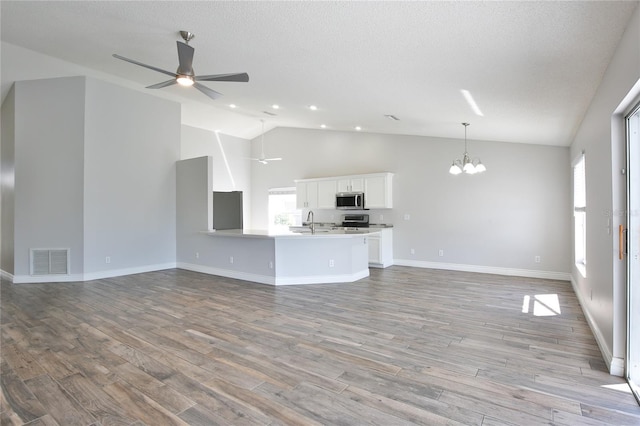 unfurnished living room with a textured ceiling, ceiling fan with notable chandelier, wood finished floors, a sink, and visible vents