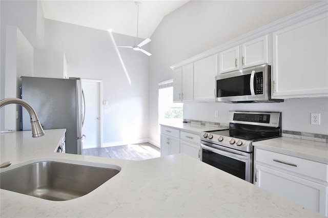 kitchen with light stone counters, stainless steel appliances, white cabinetry, a sink, and ceiling fan