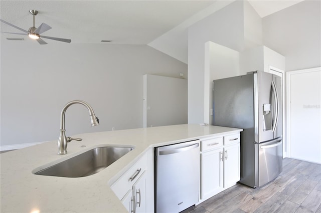 kitchen with light wood finished floors, white cabinets, appliances with stainless steel finishes, vaulted ceiling, and a sink