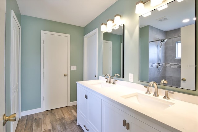 full bathroom with wood finished floors, tiled shower, a sink, and visible vents