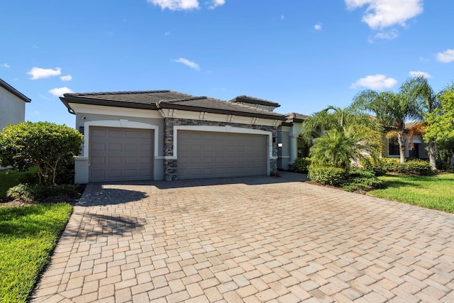 view of front of home featuring a garage, decorative driveway, a tile roof, and stone siding