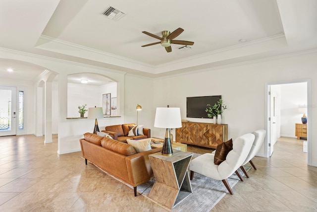 living area with arched walkways, a tray ceiling, ornamental molding, and visible vents