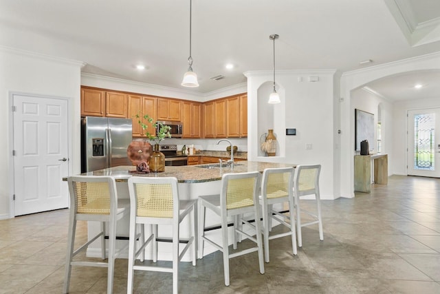 kitchen with arched walkways, appliances with stainless steel finishes, brown cabinets, a kitchen breakfast bar, and a sink