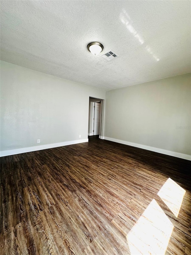 unfurnished room with a textured ceiling, wood finished floors, visible vents, and baseboards