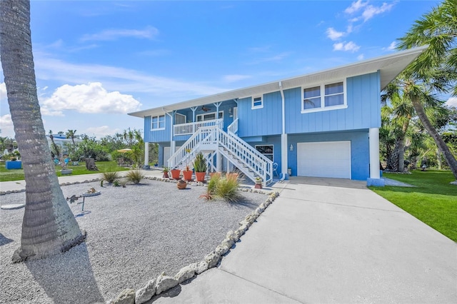 coastal inspired home with a porch, stairway, a front yard, a garage, and driveway