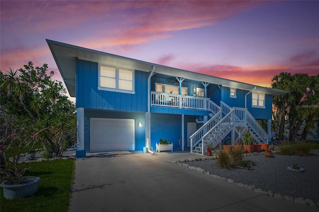 coastal home featuring a garage, covered porch, concrete driveway, and stairs