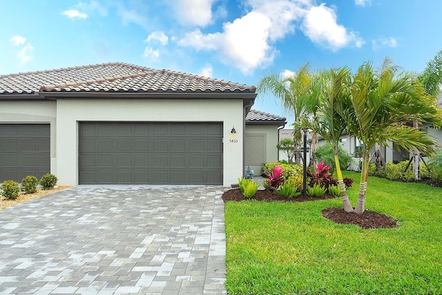 mediterranean / spanish-style home featuring decorative driveway, a tile roof, stucco siding, an attached garage, and a front lawn