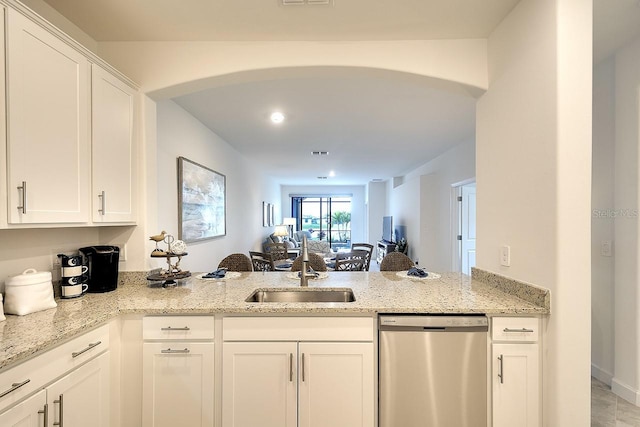 kitchen featuring arched walkways, light stone counters, a peninsula, a sink, and stainless steel dishwasher