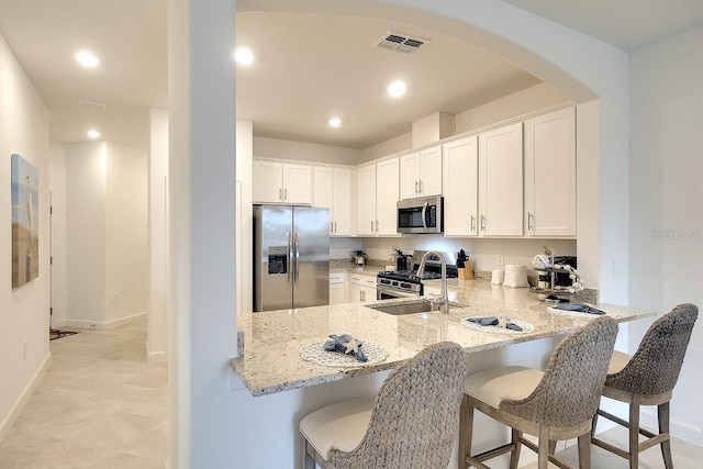 kitchen featuring light stone counters, stainless steel appliances, visible vents, a sink, and a peninsula