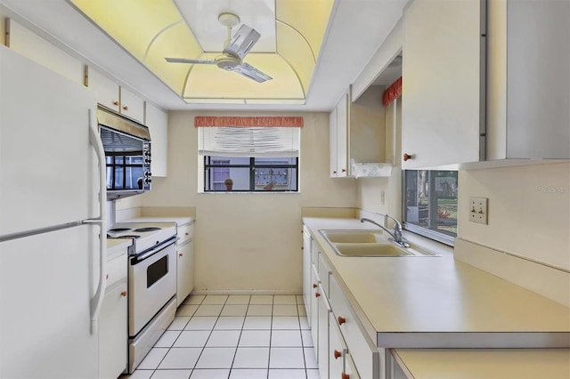 kitchen featuring a tray ceiling, white appliances, light countertops, and a sink