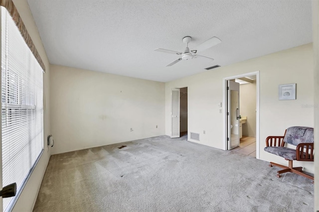 unfurnished bedroom with a textured ceiling, ceiling fan, carpet flooring, and visible vents