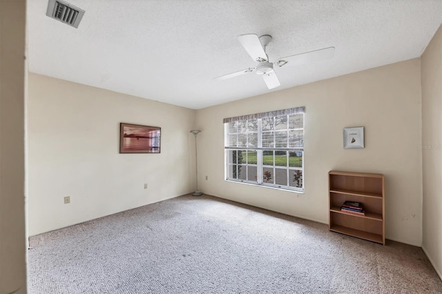 carpeted empty room with visible vents, ceiling fan, and a textured ceiling