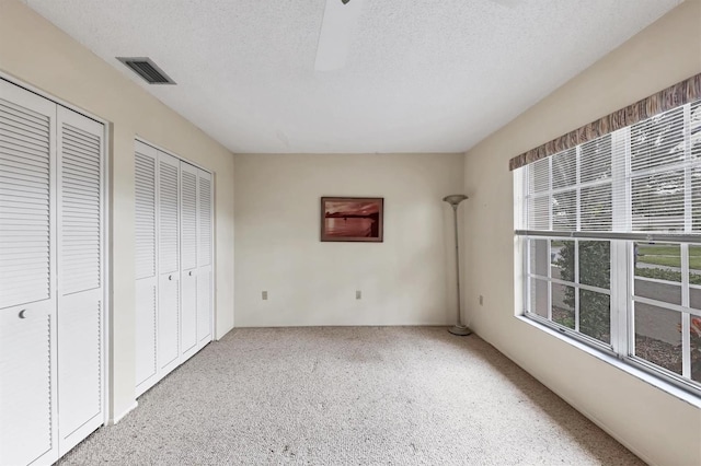 unfurnished bedroom with a textured ceiling, visible vents, two closets, and carpet flooring