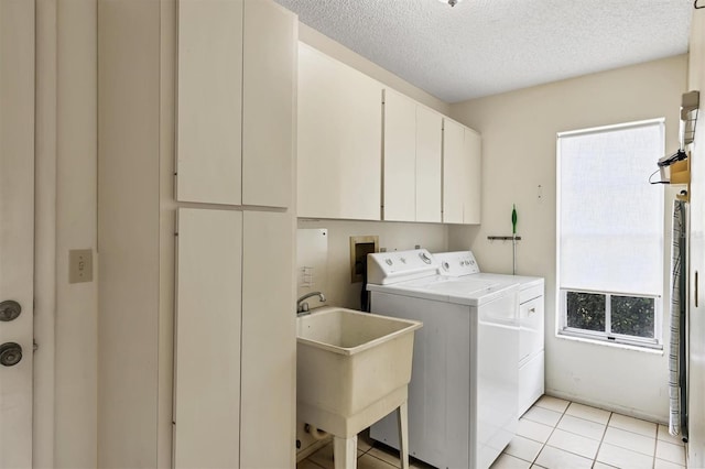 clothes washing area with cabinet space, light tile patterned floors, a textured ceiling, separate washer and dryer, and a sink