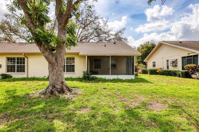 back of property with a sunroom, a shingled roof, stucco siding, and a yard