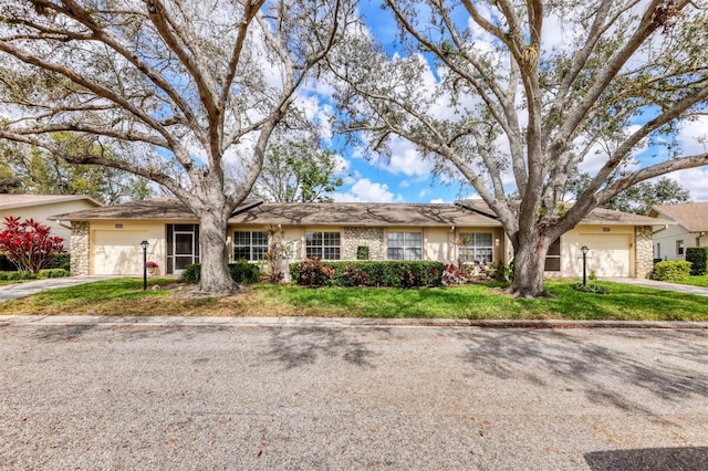 single story home featuring an attached garage, stone siding, driveway, and a front lawn