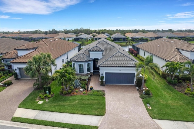 view of front of property featuring a tile roof, a residential view, an attached garage, decorative driveway, and a front lawn