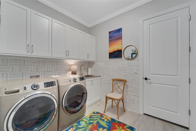 clothes washing area featuring crown molding, light wood finished floors, washing machine and clothes dryer, cabinet space, and a sink