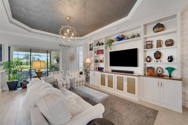 living room featuring a chandelier, light wood-style floors, built in features, a raised ceiling, and crown molding