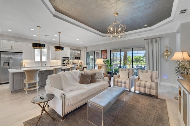 living area featuring visible vents, ornamental molding, a tray ceiling, light wood-type flooring, and a notable chandelier